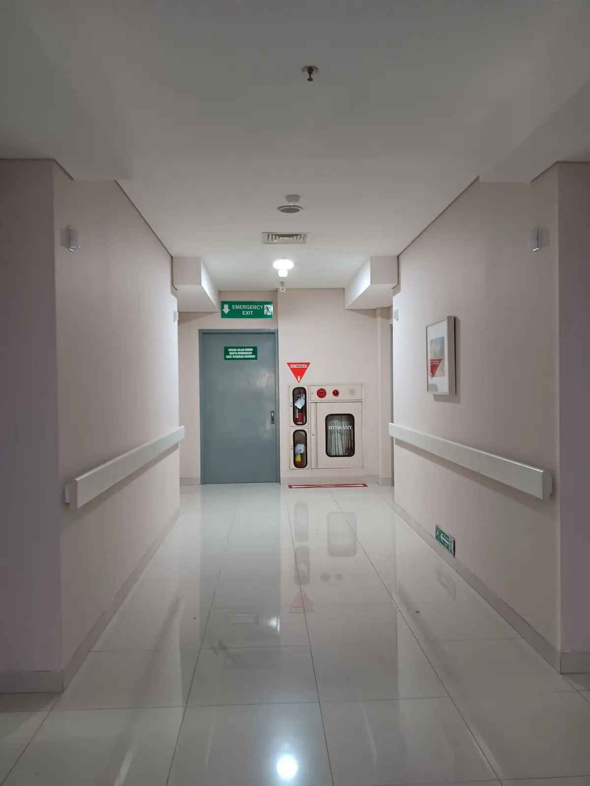 Care facility corridor with handrails leading to a marked emergency exit