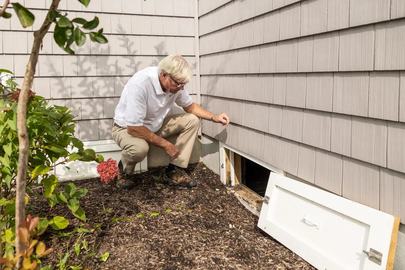 Inspector checking the crawl space access beside a home's foundation