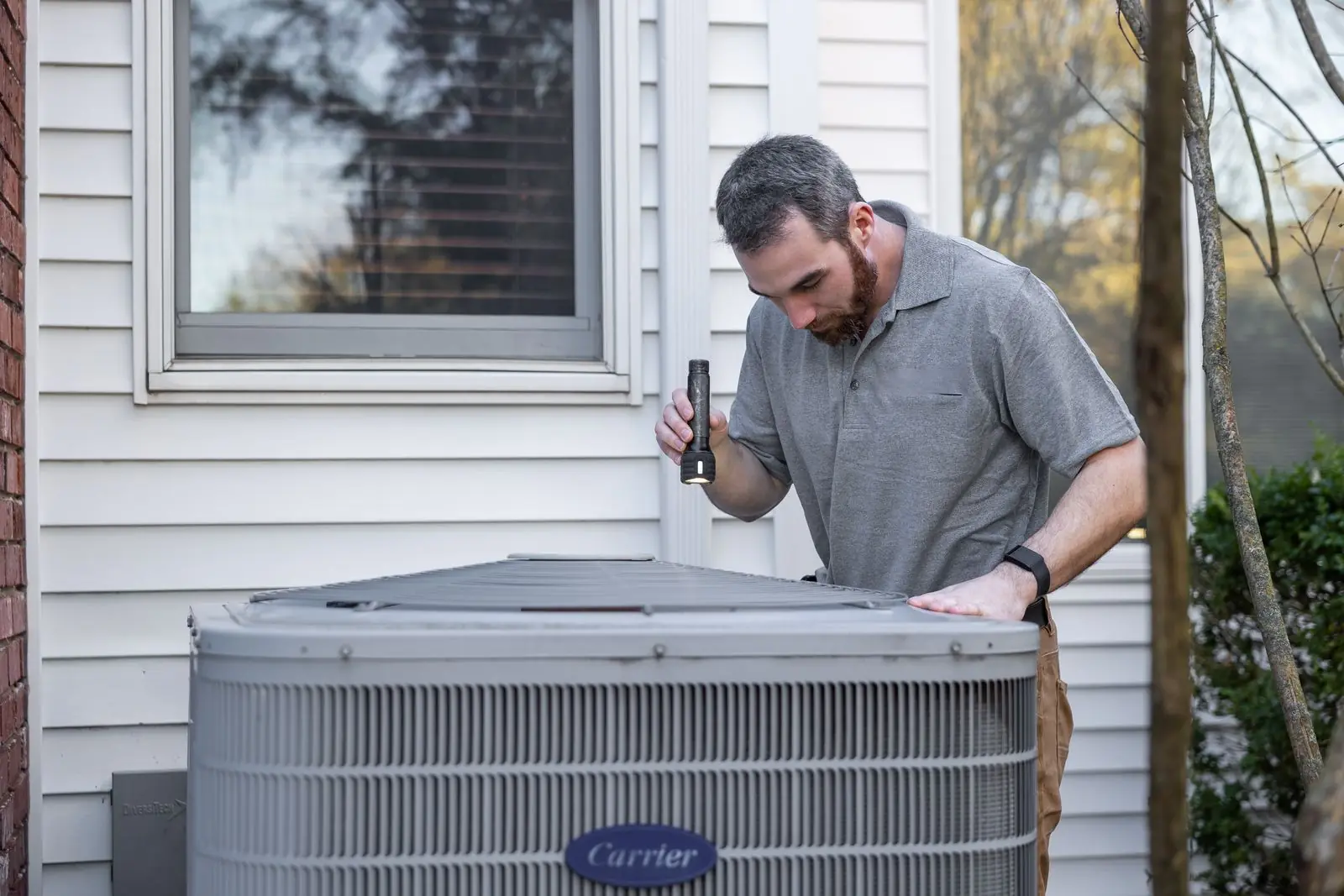 Technician inspecting an outdoor HVAC unit with a flashlight